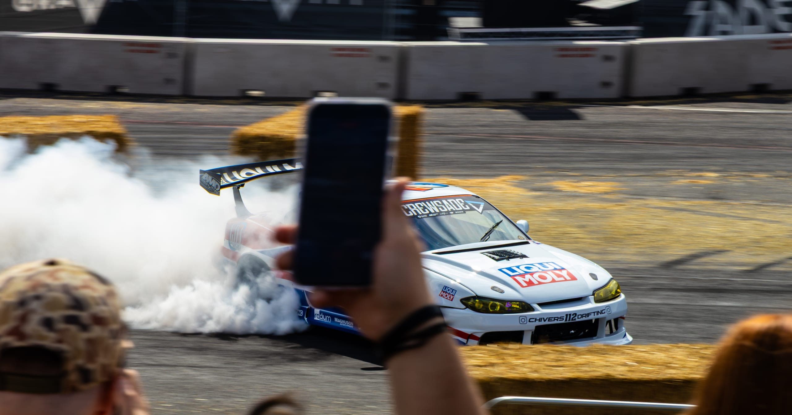 A spectator phone in the foreground as a drift car passes, Gravity 2026