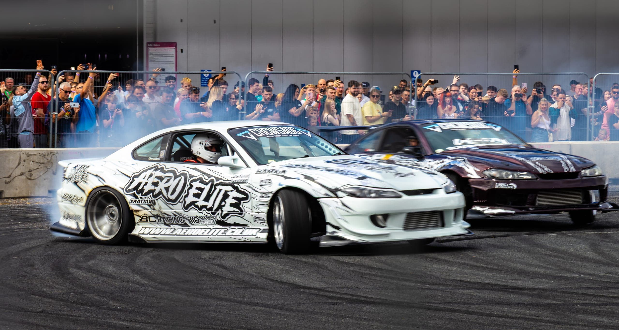 A white drift car front-on before a wall of raised phones, Gravity 2026