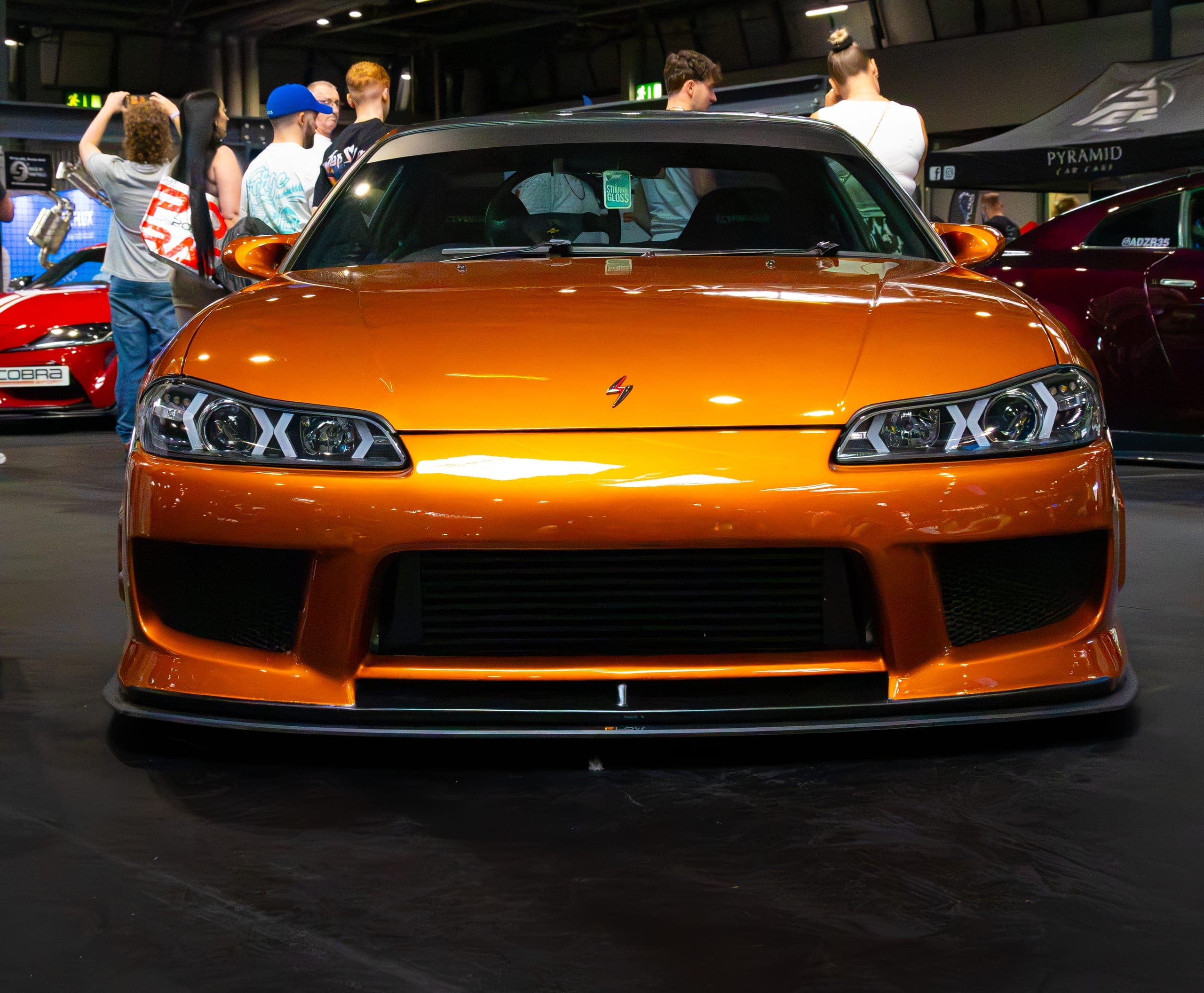 An orange show car with visitors behind it, Gravity 2026